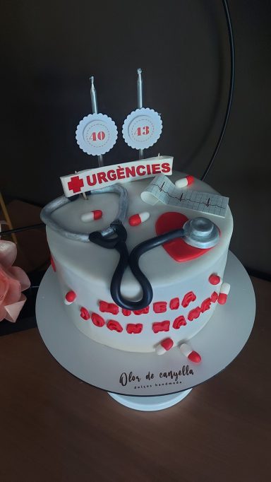 Tarta decorada con un estetoscopio, logo de urgencias y velas en forma de números.